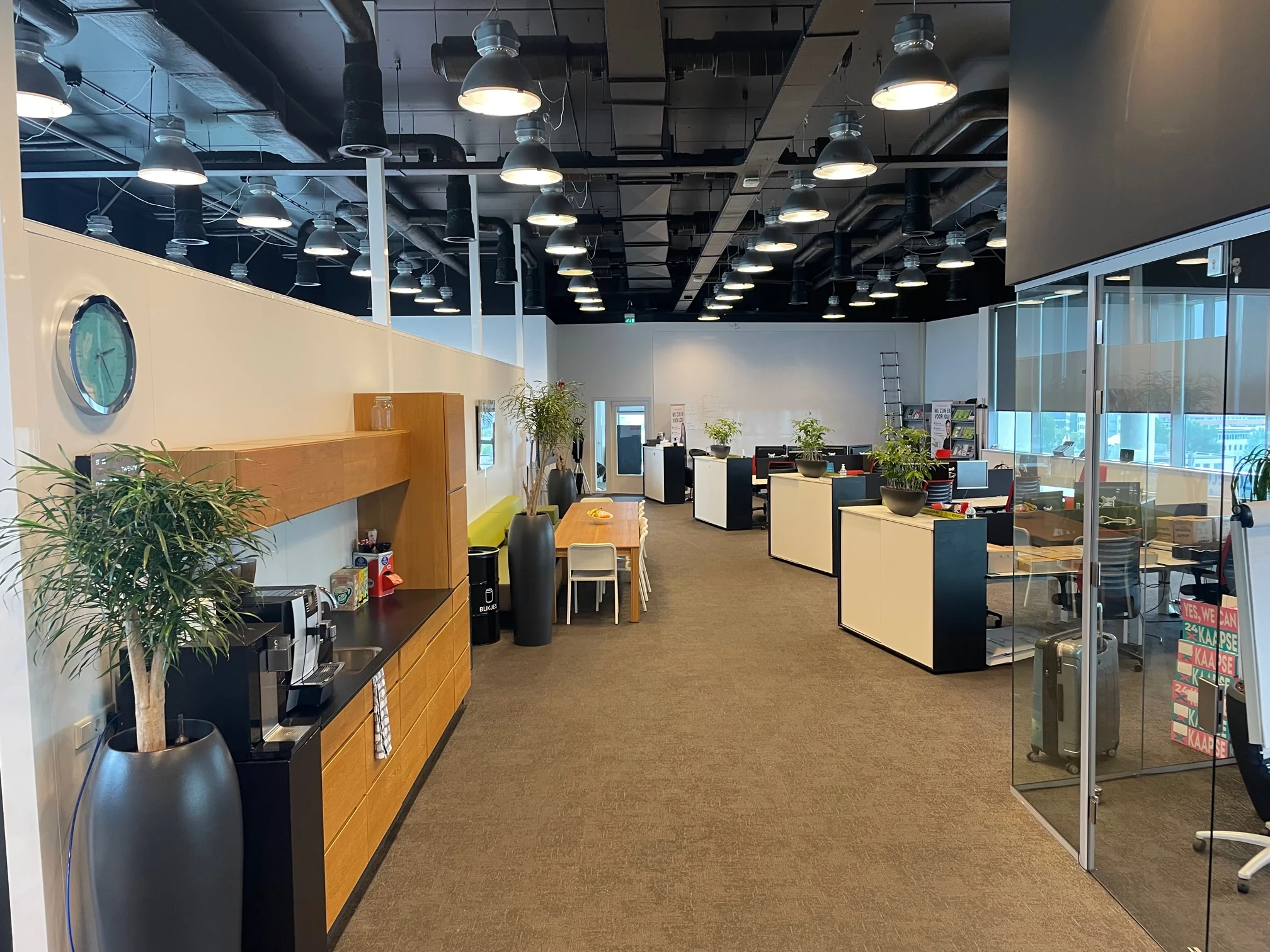 Modern kantoorinterieur op Rivium Quadrant met werkplekken, planten, een vergaderruimte en een koffiehoek.